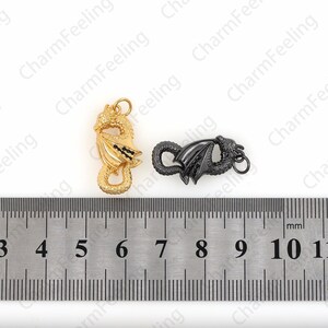 May include: Two dragon-shaped clasps, one gold and one black, are shown against a white background. A ruler is placed below the clasps, showing that each clasp is approximately 2.5 cm long.