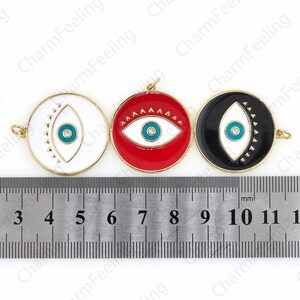 K&ouml;nnte beinhalten: Drei goldfarbene Metall-Anh&auml;nger mit einem wei&szlig;en Augenmotiv mit blauer Pupille und schwarzem Umriss. Die Anh&auml;nger haben einen Durchmesser von 2,5 cm und sind mit roter, wei&szlig;er und schwarzer Emaille verziert.