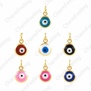 Op de afbeelding: Acht gouden boze oog bedels met verschillende gekleurde emaille inlays. De bedels zijn rond en hebben een kleine lus aan de bovenkant om aan een ketting of armband te bevestigen. De kleuren van de bedels zijn blauw, rood, wit, zwart, roze en donkerblauw.