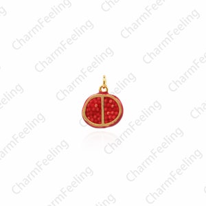 Puede incluir: Un charm con forma de granada cortada por la mitad, con borde dorado, esmalte rojo y superficie texturizada.