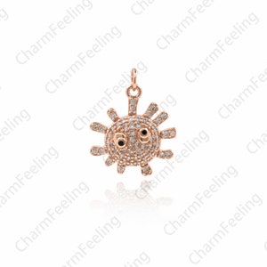 May include: A rose gold charm in the shape of a cartoon sun with sparkling clear rhinestones and black eyes.