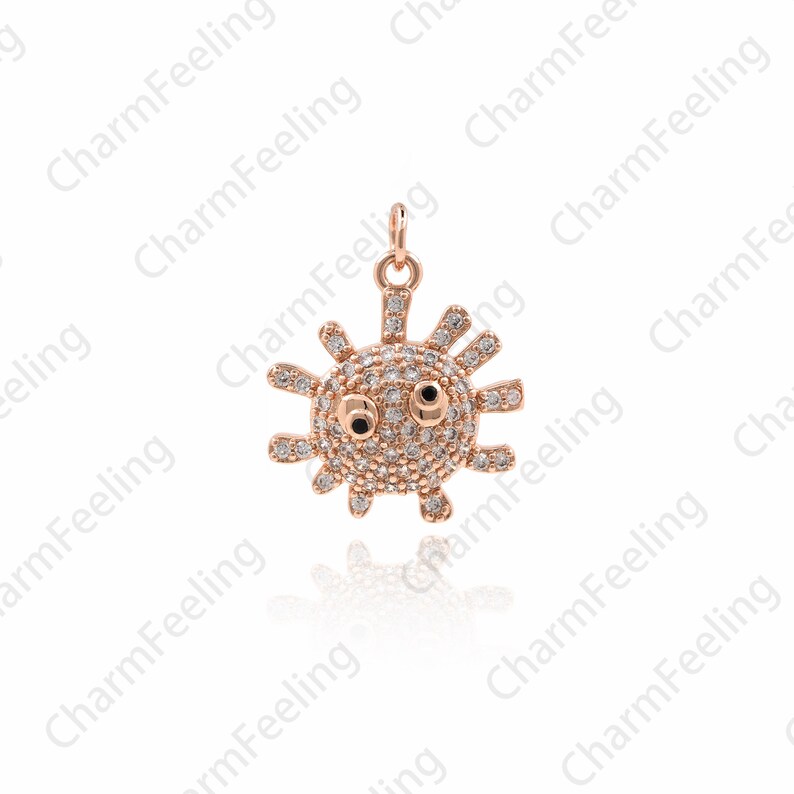 May include: A rose gold charm in the shape of a cartoon sun with sparkling clear rhinestones and black eyes.