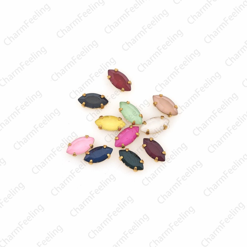 May include: Assortment of ten small, oval-shaped, glass rhinestones with gold settings. The rhinestones are in various colors, including red, pink, green, blue, yellow, and purple.