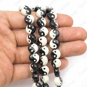 May include: A strand of black and white round beads with a yin yang symbol design. The beads are strung on a clear elastic cord.