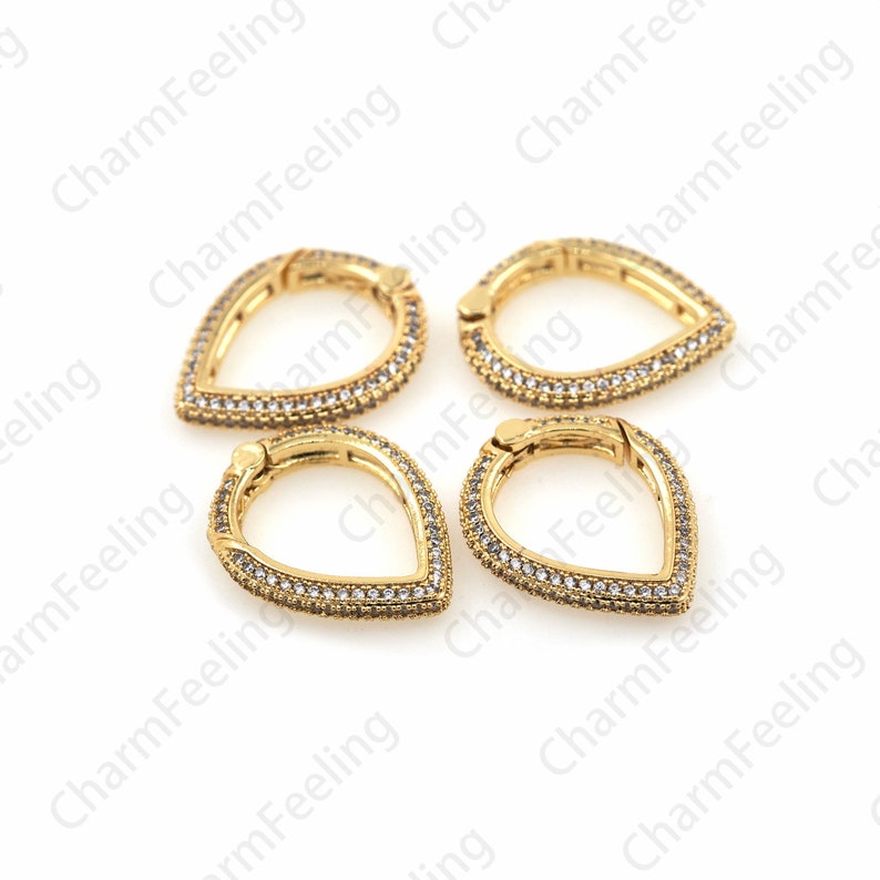 May include: Four gold-toned teardrop-shaped clasps with clear crystal embellishments. Each clasp has a hinged opening.