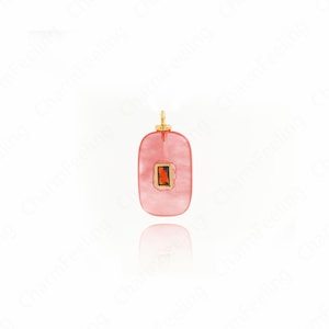 May include: A pink, rectangular pendant with a gold-coloured top and a small, rectangular, orange-coloured stone in the centre. The pendant is set against a white background.