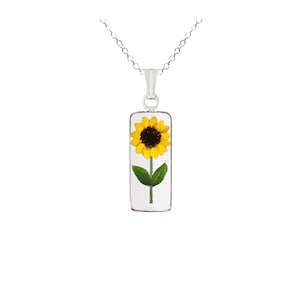 Könnte beinhalten: Eine silberne Kettenkette mit einem rechteckigen Anhänger, der eine gepresste Sonnenblume mit gelben Blütenblättern und einer dunkelbraunen Mitte zeigt.