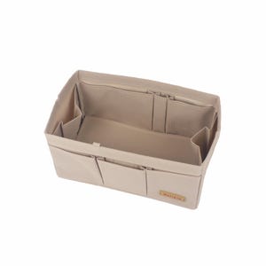 Puede incluir: Organizador de bolso de tela beige con múltiples bolsillos y compartimentos. El organizador tiene una pequeña etiqueta que dice "My Little Bag".