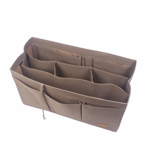 Puede incluir: Un organizador de bolso de lona beige con múltiples compartimentos y bolsillos. El organizador tiene una pequeña etiqueta marrón con la palabra "MILLER" impresa en ella.