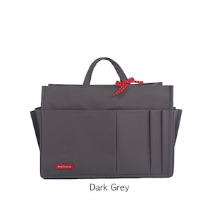 Könnte beinhalten: Ein dunkelgrauer, rechteckiger Taschenorganizer mit mehreren Außentaschen, einem Tragegriff und einer kleinen roten Schleife am Griff. Ein rotes, rechteckiges Etikett mit dem weißen Schriftzug Myllora befindet sich an der unteren linken Ecke.