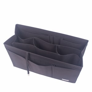 Pode incluir: Organizador de bolsa marrom escuro com vários compartimentos e bolsos. O organizador é feito de um material macio e possui um fecho de cordão. Projetado para manter os itens organizados dentro de uma bolsa ou sacola.