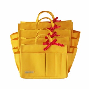 Puede incluir: Cuatro bolsas de lona amarillas con lazos de cinta de lunares rojos y blancos. Cada bolsa tiene varios bolsillos y el texto "Myloza" impreso en la parte delantera.
