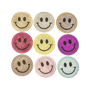 Könnte beinhalten: Neun Glitzer-Smiley-Patches in verschiedenen Farben, darunter Gold, Silber, Pink, Lila und Gelb. Die Smileys sind alle gleich groß und haben schwarze Umrisse.