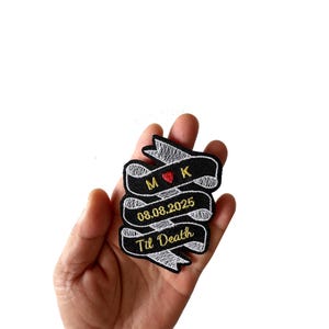 May include: Black and white embroidered patch featuring the text "M K" and a red heart, the date "08.08.2025", and "Til Death". The patch is in a banner design.