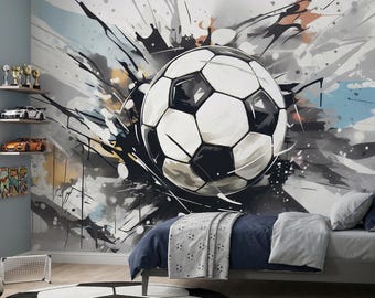 May include: A bedroom featuring a large wall mural of a black and white football with abstract paint splatters. The room includes a bed with navy bedding, a round football rug, a small football lamp, and shelves with toy cars.
