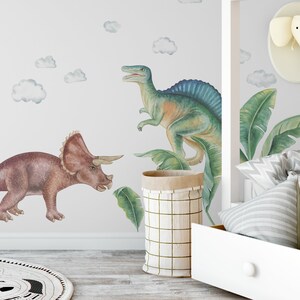 May include: Watercolor dinosaur wall decals featuring a Triceratops and a Spinosaurus in shades of brown, green, and blue. The wall art includes cloud accents, creating a playful, prehistoric theme for a child's room.