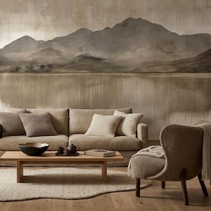 Puede incluir: Un sofá beige con cuatro cojines, una mesa de centro de madera con un cuenco oscuro y un juego de té, un sillón texturizado y una planta en maceta. La pared presenta un mural de un paisaje montañoso en tonos marrones y grises.