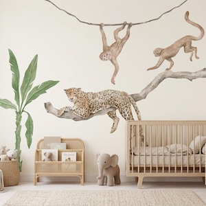 Può includere: Una cameretta a tema giungla. Una grande decalcomania da parete raffigura un leopardo, scimmie e un ramo d'albero. Una libreria in vimini, una culla e un elefante di peluche sono presenti nella stanza. La combinazione di colori è neutra con accenti verdi e marroni.