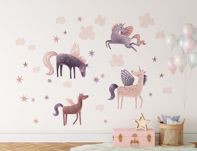 May include: Wall decals featuring whimsical unicorns with wings, in shades of purple, pink, and brown. The design includes stars and cloud shapes, creating a magical, fairytale theme. A pink trunk, star-shaped light, and balloons complete the decor.