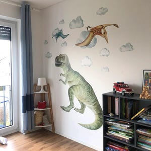 May include: A child's bedroom wall decorated with dinosaur decals. A large green Tyrannosaurus Rex is featured, along with a Pterodactyl and other flying dinosaurs, and fluffy white clouds. A red toy car sits on a shelf.