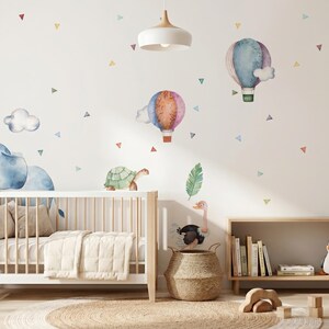 K&ouml;nnte beinhalten: Ein Kinderzimmer mit einem wei&szlig;en Kinderbett, einem Holzregal und Wandaufklebern mit einem Elefanten, Hei&szlig;luftballons und Dreiecken. Der Raum ist in sanften Pastellfarben gehalten und schafft eine beruhigende und skurrile Atmosph&auml;re. Ein kleiner Baum im Topf f&uuml;gt einen Hauch von Natur hinzu.