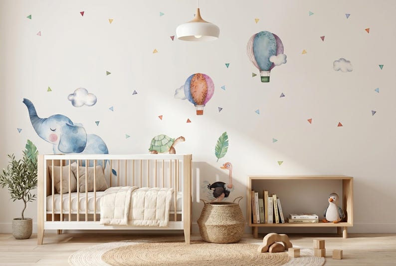 K&ouml;nnte beinhalten: Ein Kinderzimmer mit einem wei&szlig;en Kinderbett, einem Holzregal und Wandaufklebern mit einem Elefanten, Hei&szlig;luftballons und Dreiecken. Der Raum ist in sanften Pastellfarben gehalten und schafft eine beruhigende und skurrile Atmosph&auml;re. Ein kleiner Baum im Topf f&uuml;gt einen Hauch von Natur hinzu.