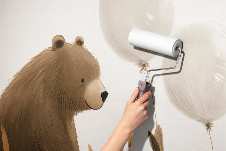 May include: A wall mural featuring a brown bear illustration next to light beige balloons. A white paint roller is being used to apply the mural to the wall surface. The bear has dark brown fur, a tan muzzle, and a black nose, while the balloons are depicted with soft, brush-like strokes.