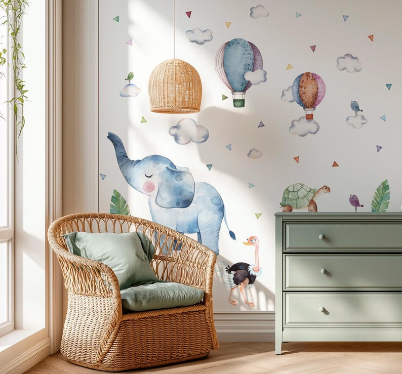 K&ouml;nnte beinhalten: Ein Kinderzimmer mit einem Korbsessel, einem gr&uuml;nen Kissen und einem gr&uuml;nen Kissen. Die Wand ist mit Aquarellillustrationen eines blauen Elefanten, Hei&szlig;luftballons, Wolken und Tieren geschm&uuml;ckt. Eine gr&uuml;ne Kommode und eine Pendelleuchte aus Korbgeflecht sind ebenfalls zu sehen.