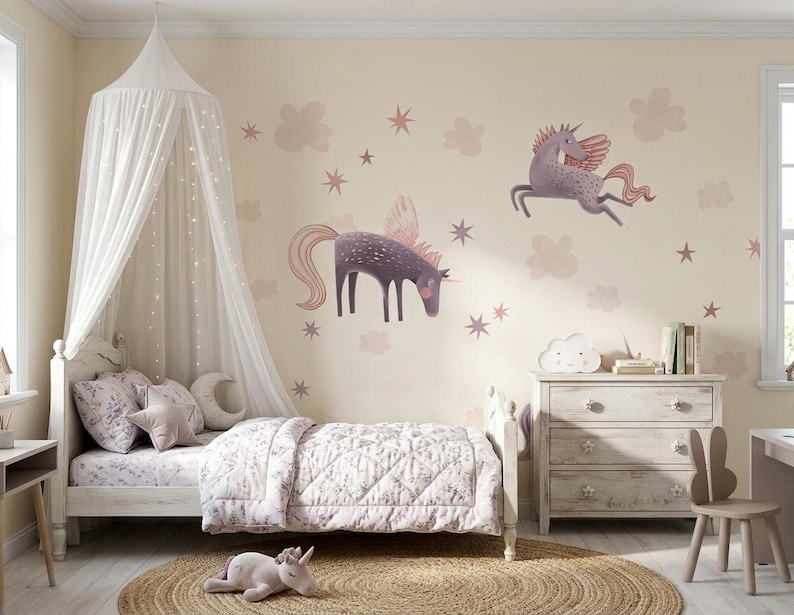May include: A child's bedroom with a white bed, canopy, and dresser. The walls are decorated with unicorn decals, clouds, and stars. The bed has floral bedding and decorative pillows. A stuffed unicorn is on the floor.