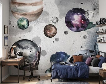 May include: A wall mural featuring a watercolor space theme with various planets, moons, and nebulae in shades of blue, purple, brown, and gray against a textured light gray background with scattered dark paint splatters and cosmic dust effects.