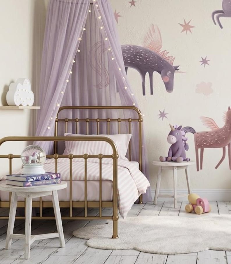 May include: A child's bedroom with a gold metal bed frame, a canopy, and unicorn-themed decor. The room features a white rug, a small side table, and a plush unicorn toy. The walls are painted a light beige with unicorn wall decals.