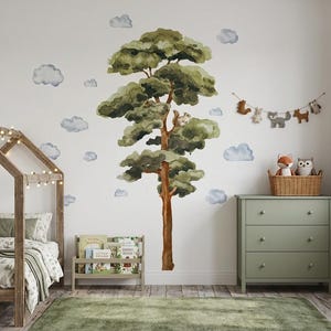 Könnte beinhalten: Ein Kinderzimmer mit einem holzförmigen Bett, einer grünen Kommode und einem Wandbild eines Baumes und Wolken. Eine Girlande aus Filztieren hängt über der Kommode. Ein Korb enthält einen Stofffuchs und eine Eule.