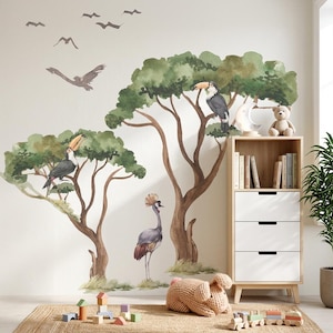 Peut inclure: Décoration de chambre d'enfant avec des décalcomanies murales à l'aquarelle représentant des toucans, des arbres et des oiseaux. Une bibliothèque en bois avec des livres et un ours en peluche se trouve à côté de l'art mural. Un tapis tissé et des jouets en bois complètent le décor.