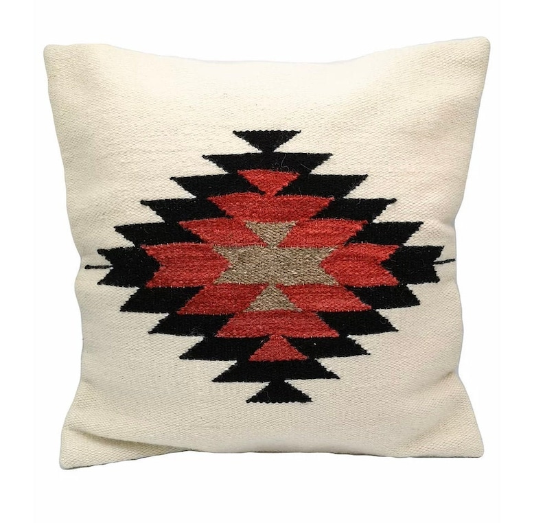 Pu&ograve; includere: Cuscino bianco con un motivo geometrico rosso, nero e marrone. Il motivo &egrave; una forma di diamante stilizzata con una stella al centro.