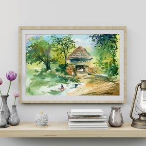 May include: A watercolor painting of a small, rustic house with a thatched roof, surrounded by lush green trees and a stream. The painting is framed in a light wood frame and is displayed on a shelf with other decorative items.