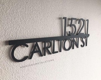 Puede incluir: Un letrero de dirección de metal negro con los números "1521" sobre el nombre de la calle "CARLTON ST". El letrero está montado en una pared blanca texturizada. El texto "#DESIGNSMETALSTORE" está en la parte inferior.