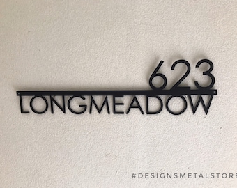 Puede incluir: Un letrero de metal negro para casa que muestra el número 623 sobre una barra horizontal, con la palabra LONGMEADOW en letras mayúsculas debajo. El letrero incluye pequeños orificios de montaje en cada extremo de la barra.
