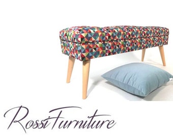 May include: A colorful geometric patterned storage bench with wooden legs and a light blue throw pillow. Rossi Furniture.