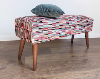 May include: A colorful patterned storage bench with wooden legs and a teal velvet cushion on top.