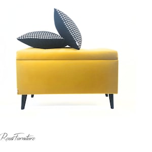 May include: A yellow storage ottoman with black legs and two black and white patterned throw pillows on top.