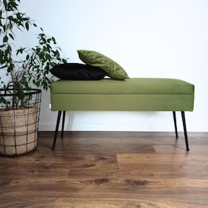 May include: A green velvet storage bench with black metal legs. The bench has two black pillows on top.