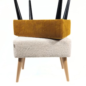 Peut inclure: Un tabouret à deux niveaux avec une assise en velours côtelé jaune moutarde et une assise texturée crème. La partie supérieure a des pieds noirs et la partie inférieure a des pieds en bois clair. Le tabouret est sur fond blanc.