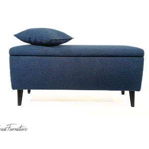 May include: A blue upholstered storage bench with a matching blue cushion. The bench has black wooden legs.