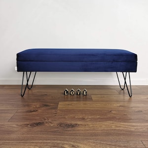 May include: A navy blue velvet storage bench with black hairpin legs. The bench is sitting on a wood floor with the word "LOVE" spelled out in black blocks.