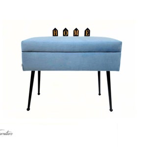 May include: A light blue storage ottoman with black metal legs. The ottoman has a rectangular top with the word "HOME" spelled out in black letters with gold trim.
