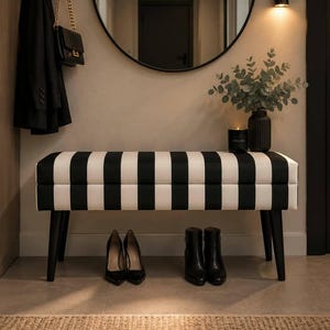 Può includere: Una panca rettangolare con seduta imbottita a strisce verticali bianche e nere e quattro gambe nere affusolate. La panca è posizionata in un ingresso con un paio di décolleté nere e un paio di stivaletti neri riposti nella parte sottostante.