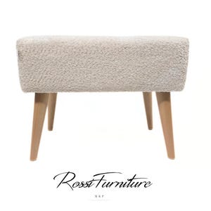 Puede incluir: Un otomán rectangular tapizado en blanco roto con una superficie texturizada. El otomán tiene cuatro patas de madera clara en ángulo. La marca "Rossi Furniture" está escrita en cursiva en la parte inferior.