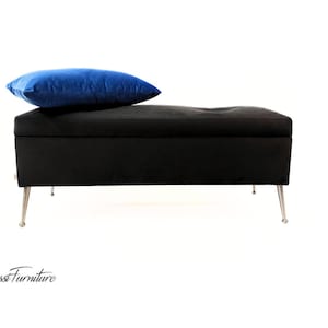May include: A black velvet storage bench with silver legs and a blue velvet pillow on top.
