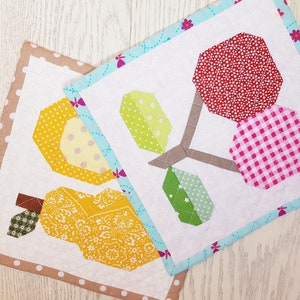 May include: Two fabric squares with a patchwork design. One square features a yellow pear with a brown stem and green leaves. The other square features a brown tree with three red, pink, and green fruit.