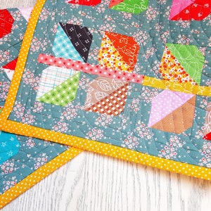 May include: A patchwork quilt with a teal background and a yellow border. The quilt is made up of various colorful squares and triangles, including red, orange, yellow, green, blue, pink, and brown. The quilt is quilted with a curved design.